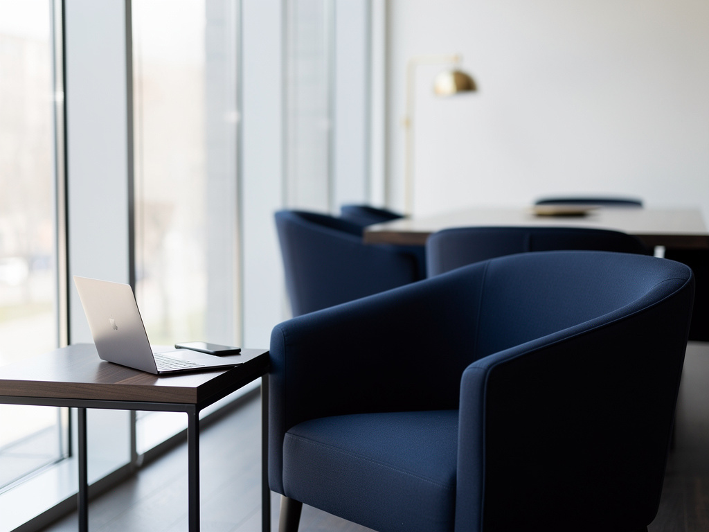 The studio entrance with a navy armchair, a side table holding a phone and an open laptop, and soft daylight, no one in 